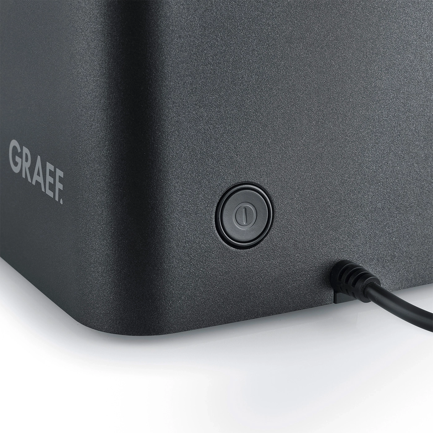 Close-up of a Graef appliance with a button and cable, black background, detailed shot