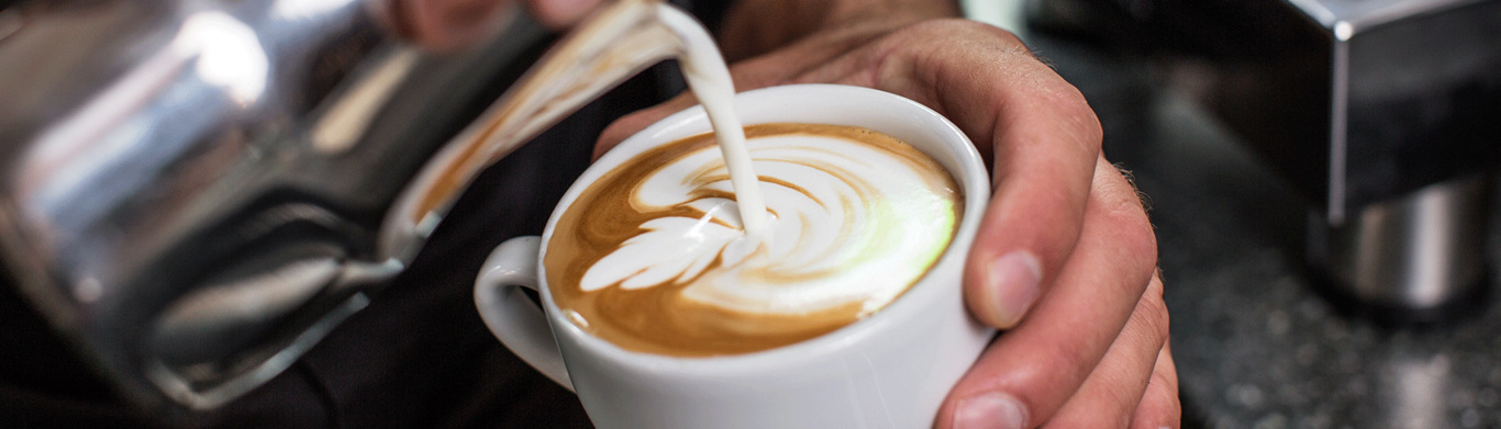 Nahaufnahme eines Baristas, der Milch in eine Tasse Kaffee gießt, um Latte Art zu kreieren.