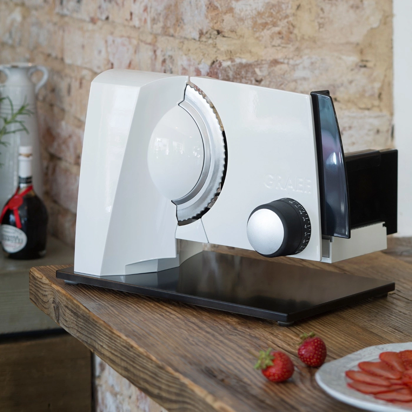 Elektrische Aufschnittmaschine auf einem Holztisch mit Erdbeeren und Ziegelwand.