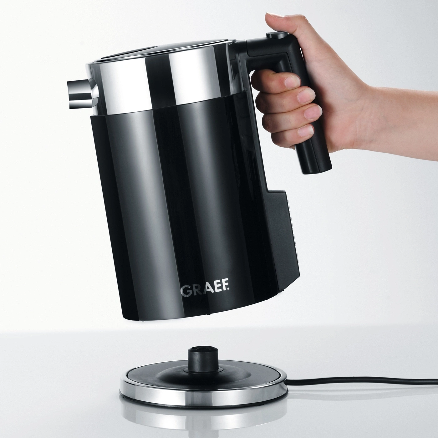 Schwarzer Wasserkocher wird von einer Hand gehalten, die über einer Basis schwebt.