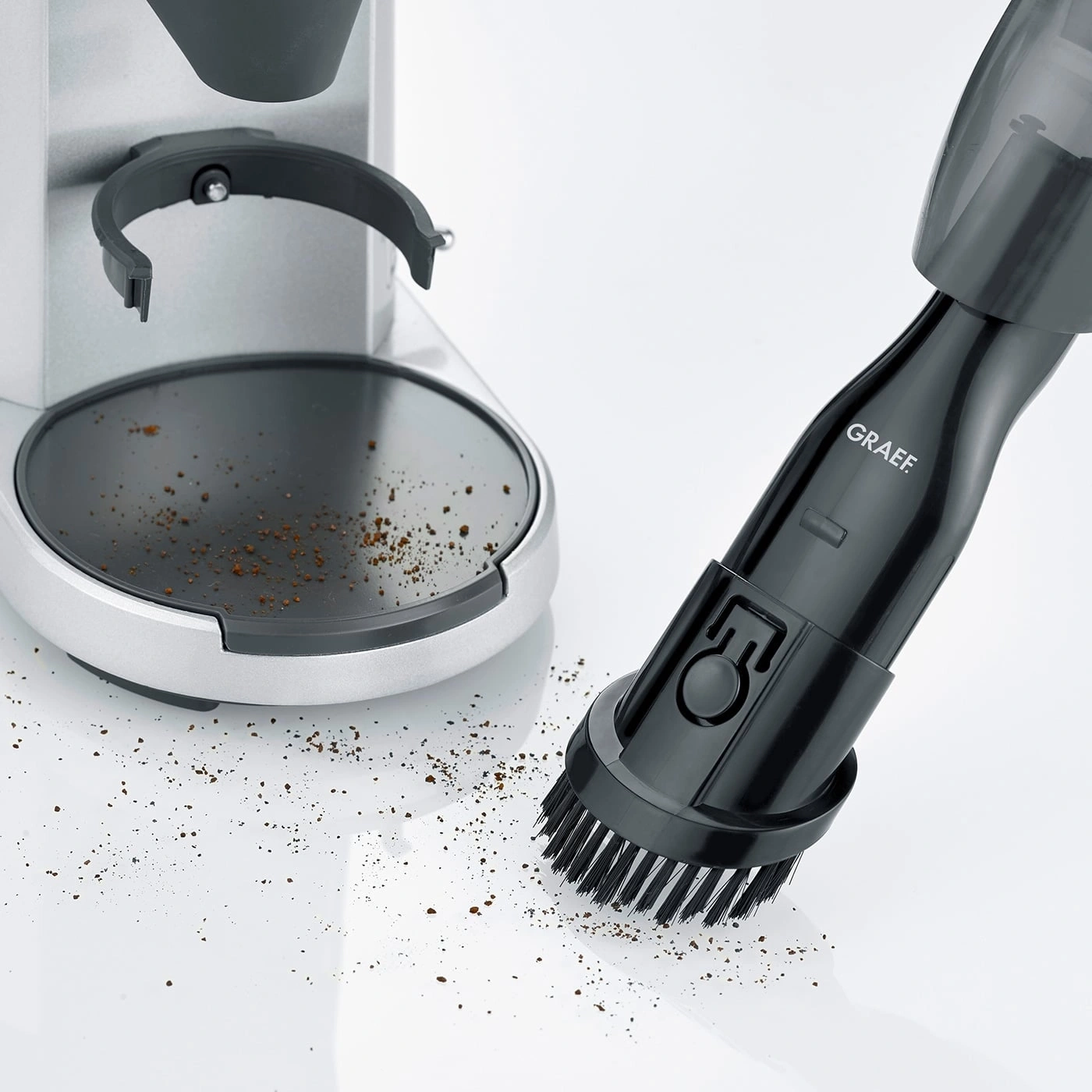 Moulin à café et aspirateur avec brosse nettoyant le marc de café sur fond blanc.