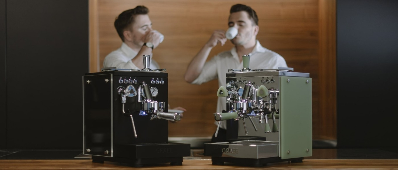 Zwei Männer trinken Kaffee, neben ihnen stehen Espressomaschinen.