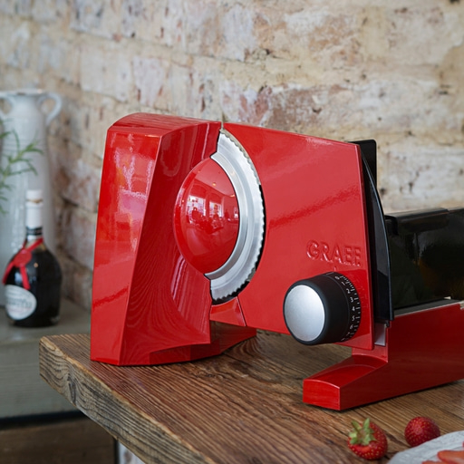 Roter Aufschnittschneider auf Holzoberfläche mit Erdbeeren und Flasche im Hintergrund.