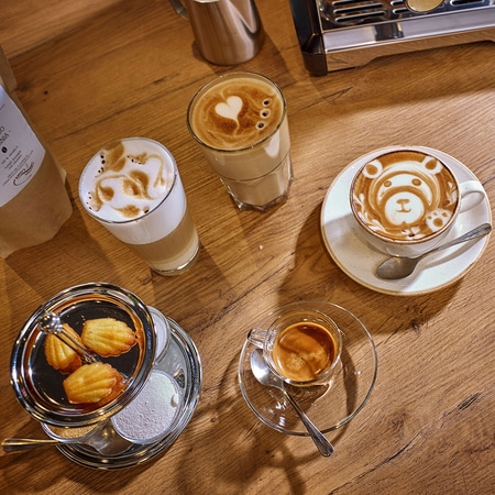 Kaffee-Kunst mit Gebäck auf einem Holztisch. Latte, Espresso und Kuchen.