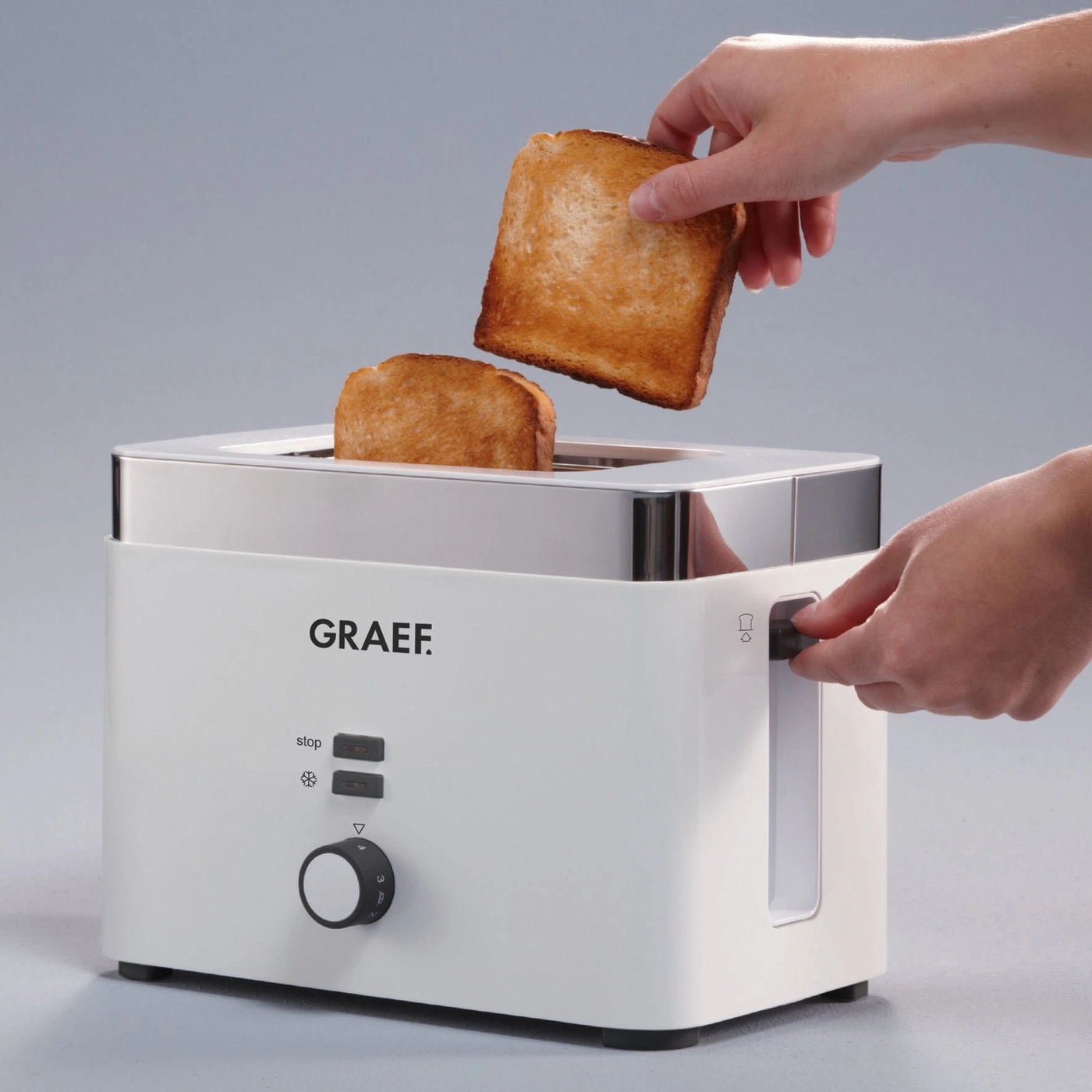 White toaster with toast being removed and a hand turning the knob, ready to eat breakfast.