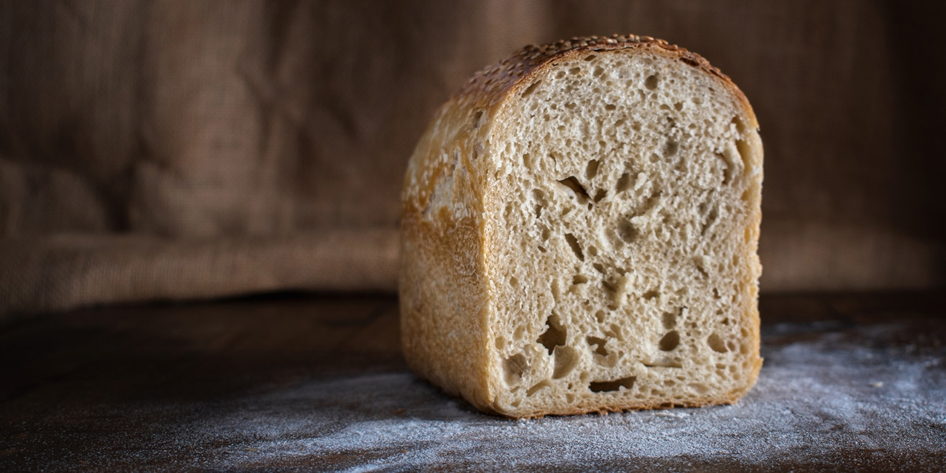 A loaf of bread, dusted with flour, resting on a wooden surface.
