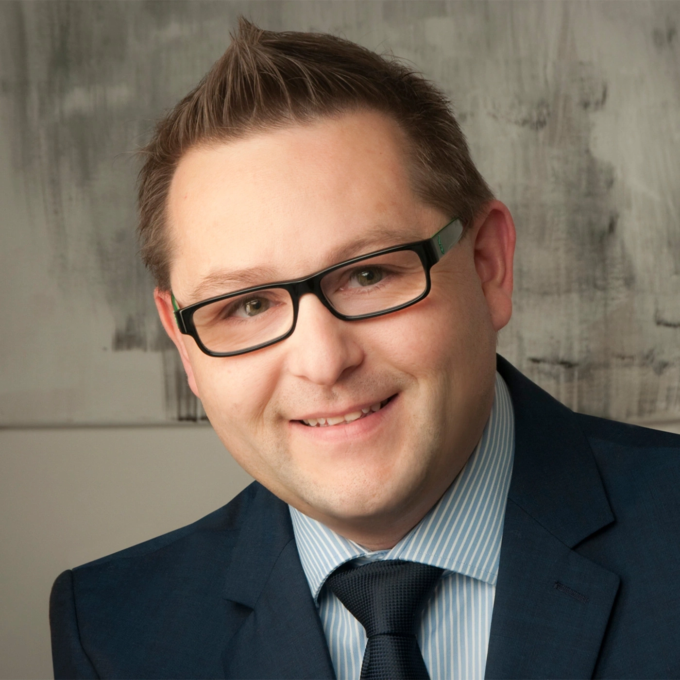 Ein Mann mit Brille lächelt in die Kamera, Anzug und Krawatte.