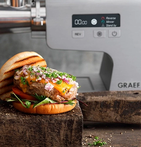 Burger with cheese and onions in front of a meat grinder machine