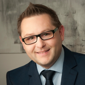 Ein Mann mit Brille lächelt in die Kamera, Anzug und Krawatte.