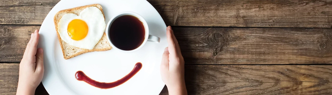 Frühstück mit Spiegelei in Herzform, Kaffee und Ketchup-Lächeln auf Holzuntergrund