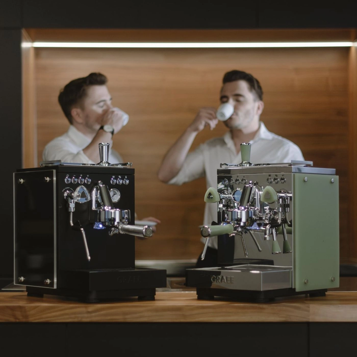 Zwei Männer trinken Kaffee neben Espressomaschinen.