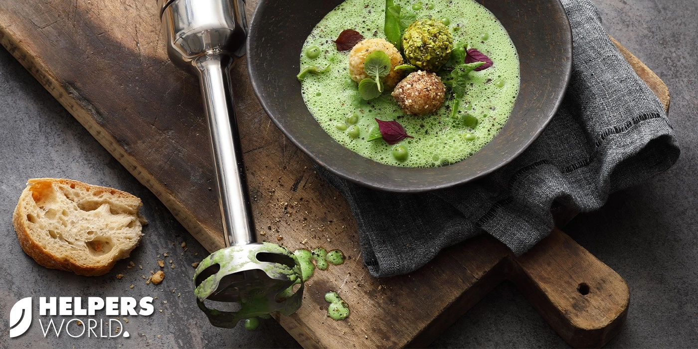 Green soup with bread and immersion blender on wooden board