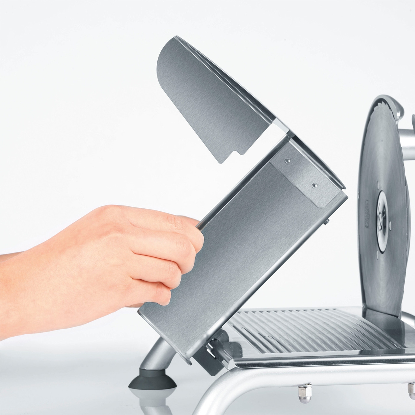 Close-up of a meat slicer with the guard open, held by a hand, stainless steel.