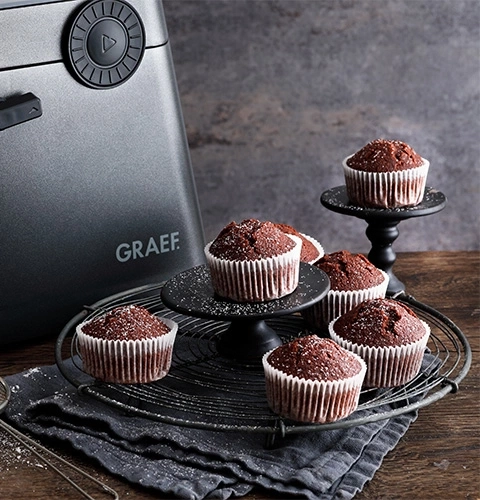 Chocolate muffins on a wire rack and black stands with a GRAEF appliance in the background