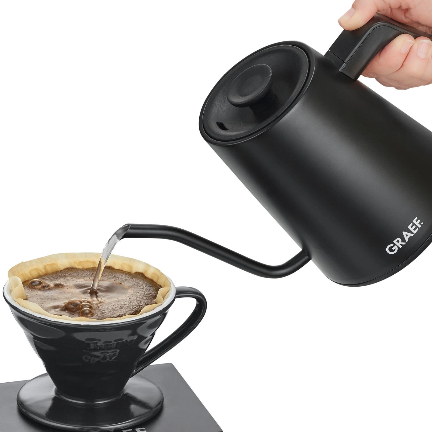 Black kettle pouring coffee into a cup with a filter, brewing process.