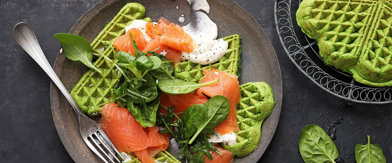 Grüne Waffeln mit Lachs, Salat und Sauce auf einem Teller.