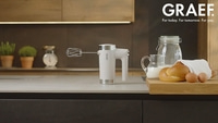 Kitchen scene with hand mixer, bread, eggs, and milk. GRAEF logo.