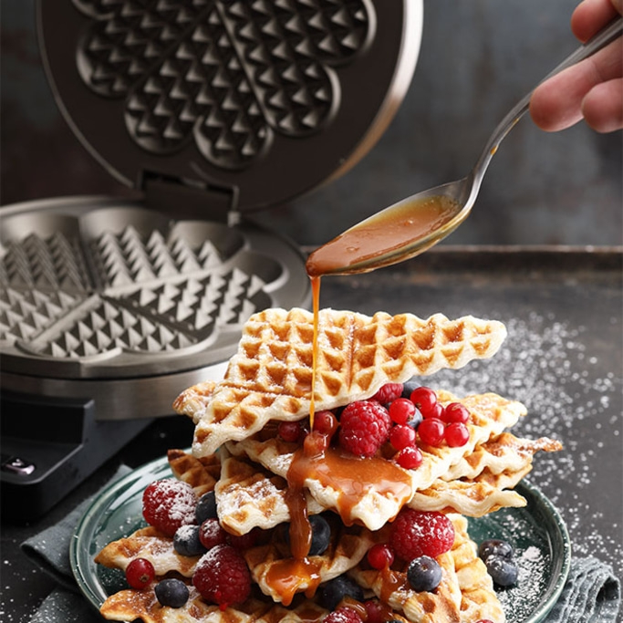 Waffeln mit Beeren und Sirup, die von einer Gabel gegossen werden, mit Waffeleisen.
