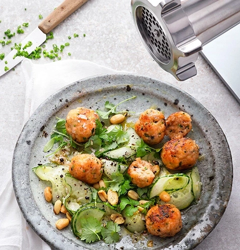 Meatball salad with peanuts and cucumbers on a plate with a knife and meat grinder
