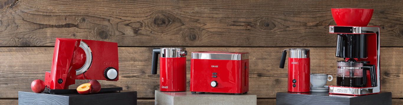 Red kitchen appliances on wooden background: toaster, coffee machine, milk frother, etc.