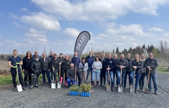 Gruppe von Menschen mit Spaten vor Bäumen und blauem Himmel.