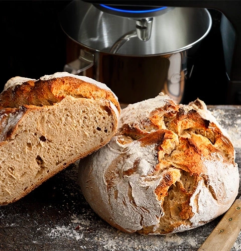Sliced loaf of bread on wooden board with kitchen machine in background