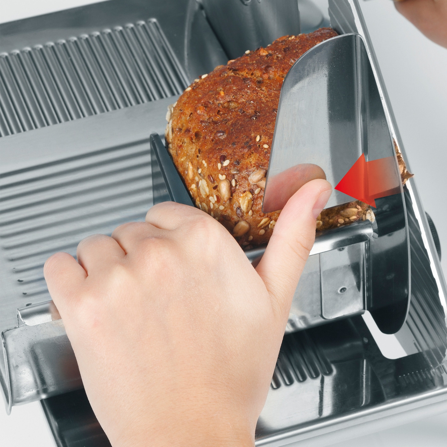 Bread being sliced with a slicer, close-up of hand and bread.