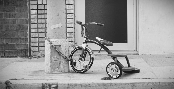 Schwarzweiß-Foto eines Dreirads, das an einer Säule mit Kette befestigt ist.