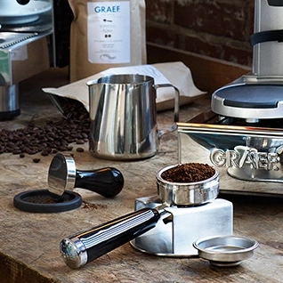 Kaffeemaschine mit Zubehör, Kaffeebohnen und Milchkanne auf Holzoberfläche