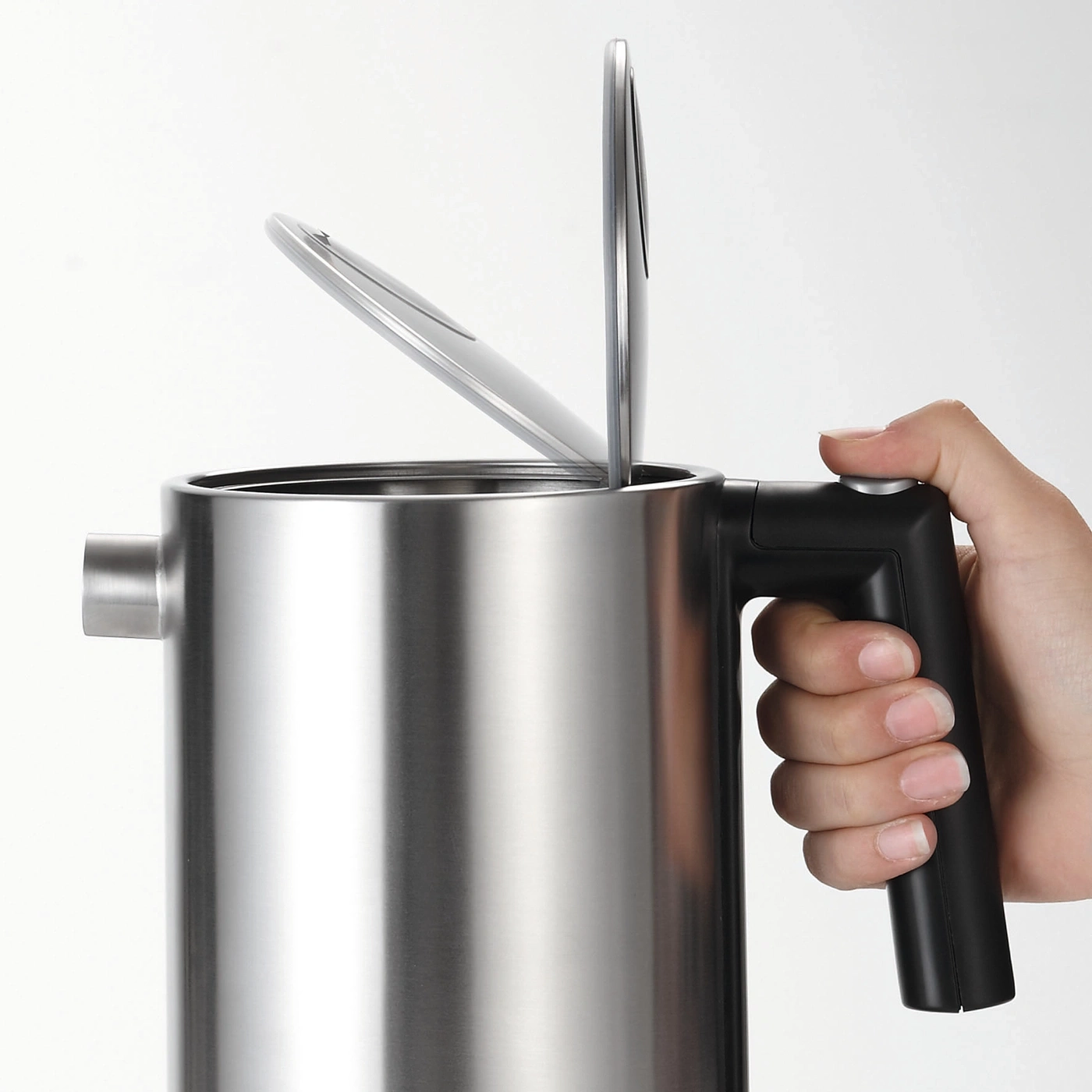 Stainless steel kettle with open lid held by a hand, close-up shot, white background.