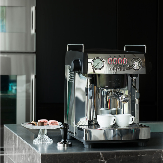 Espresso machine with cups, macarons, and tamper on a countertop.