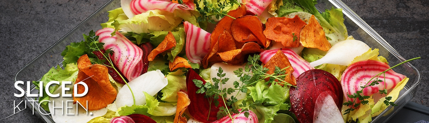 Colorful salad with vegetable chips and fresh herbs in a transparent container.