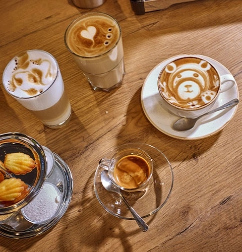 Kaffee mit Latte Art, Gebäck und Espresso auf einem Holztisch