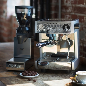 Kaffeemaschine und Kaffeemühle auf einem Holztisch mit Süßigkeiten und Kaffeebecher