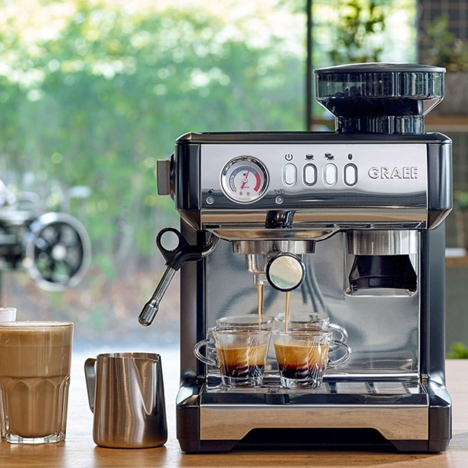 Machine à expresso avec deux tasses, pichet à lait et un verre de café