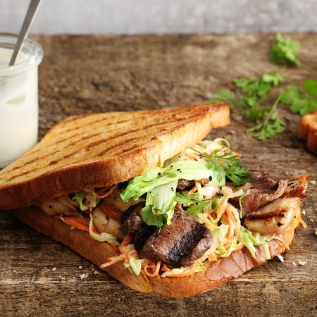 Gegrilltes Sandwich mit Fleisch, Gemüse und Salat auf Holzuntergrund