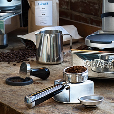 Kaffeemaschine mit Zubehör, Kaffeebohnen und Milchkanne auf Holzoberfläche