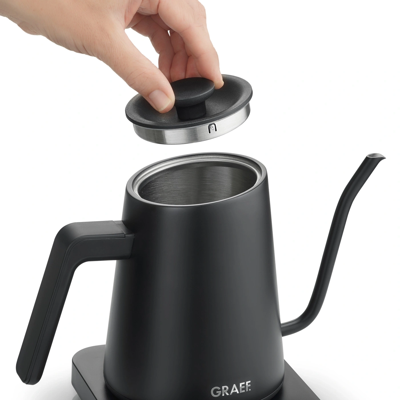 Black kettle with removable lid being held by a hand, close-up shot, white background.