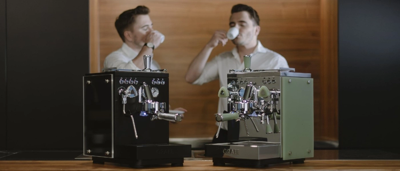 Zwei Männer trinken Kaffee, neben ihnen stehen Espressomaschinen.