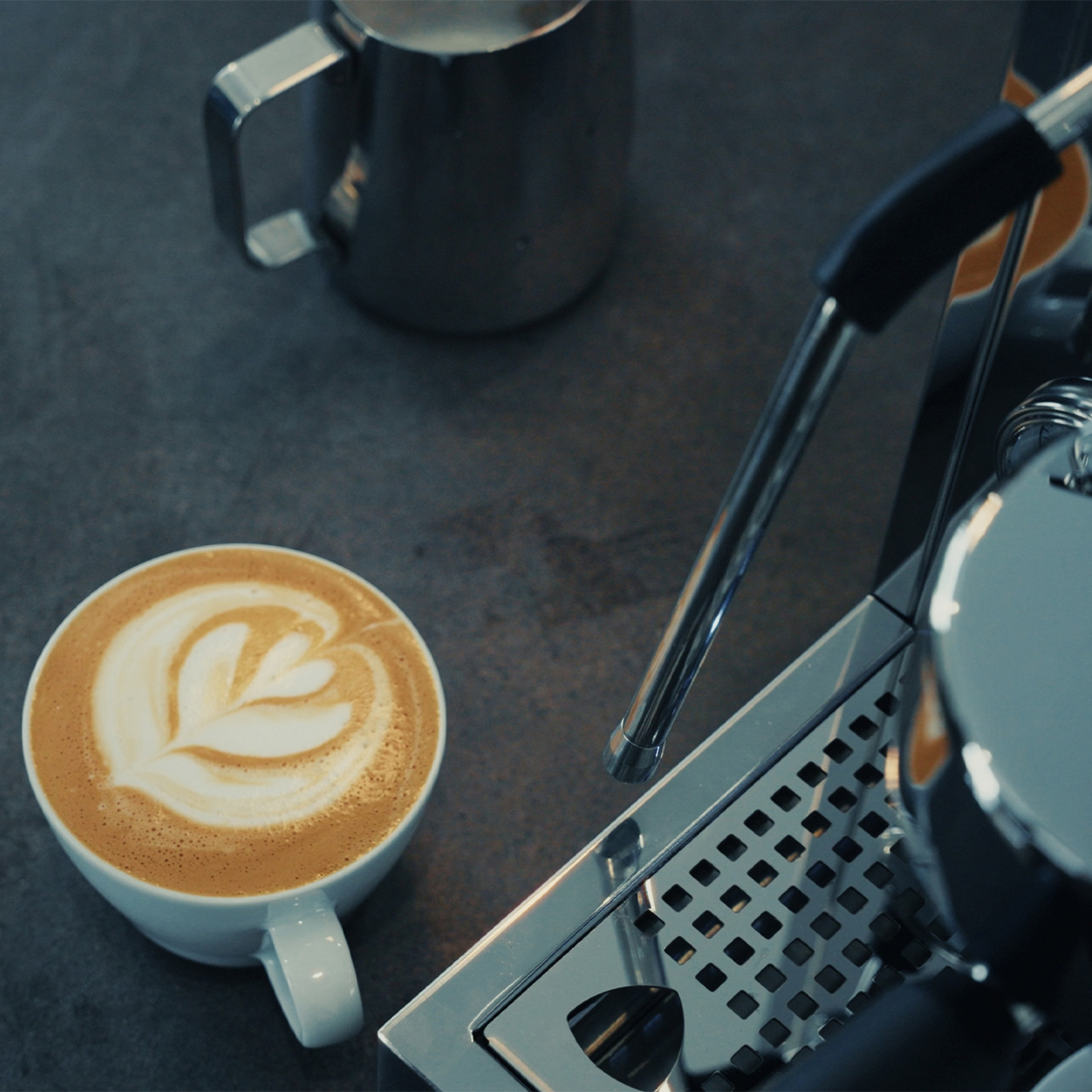 Eine Tasse Latte Art Kaffee neben einer Espressomaschine und einem Milchbehälter.