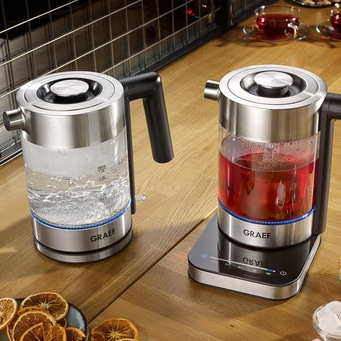 Zwei elektrische Wasserkocher mit Wasser und Tee auf einem Holztisch, GRAEF-Marke.