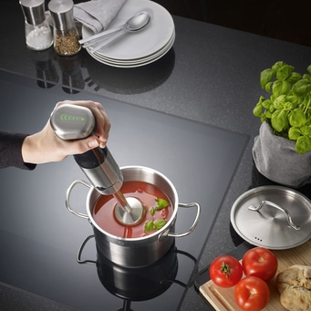 Handmixer in einem Topf mit Tomatensuppe, Basilikum und Tomaten.