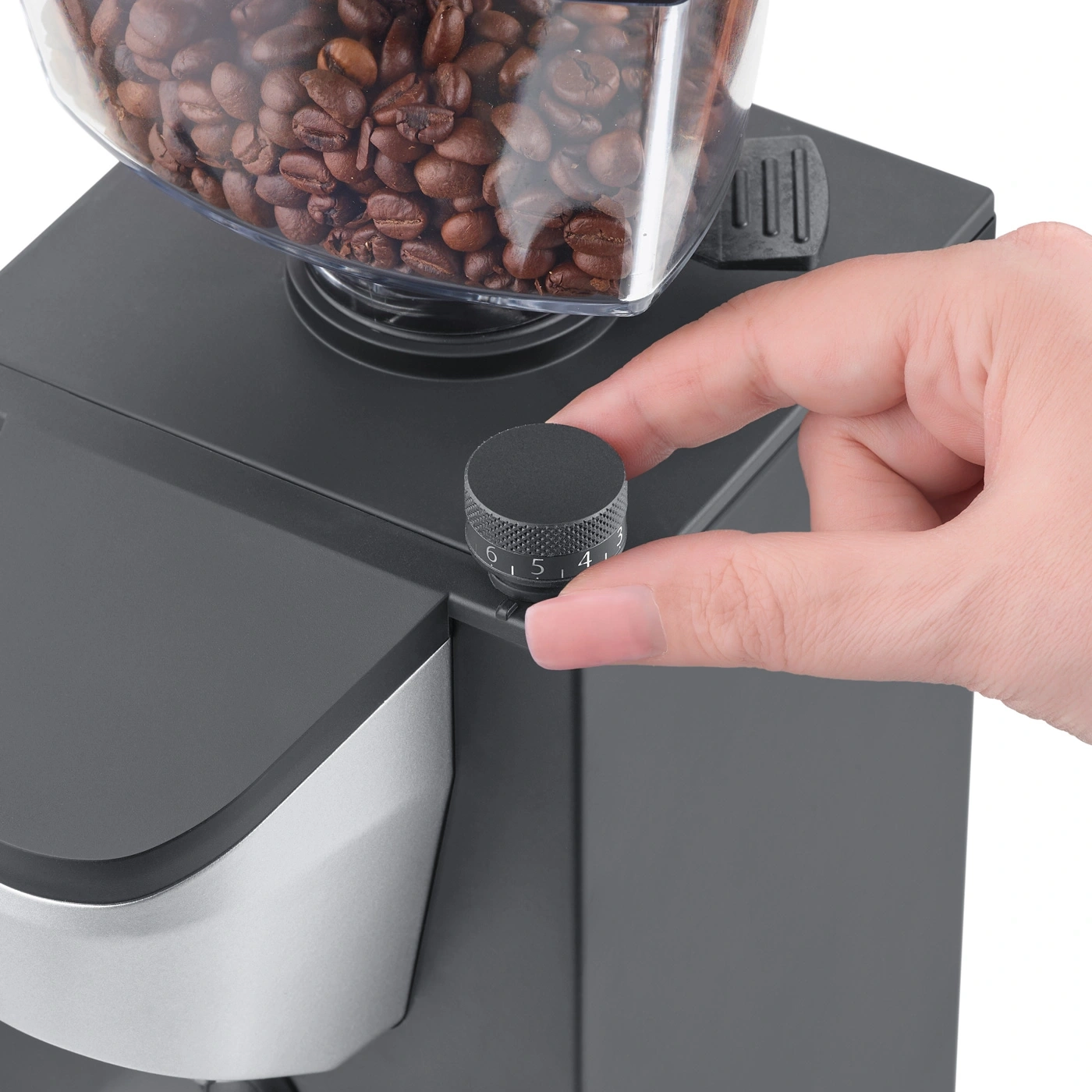 Main tournant un bouton noir sur un moulin à café avec des grains de café