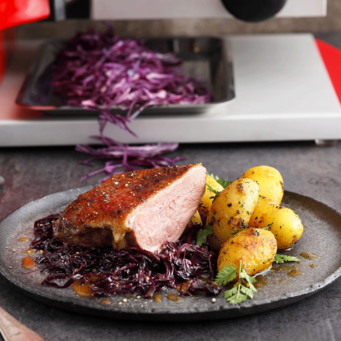 Gebratene Ente mit Rotkohl und Kartoffeln auf einem Teller serviert.