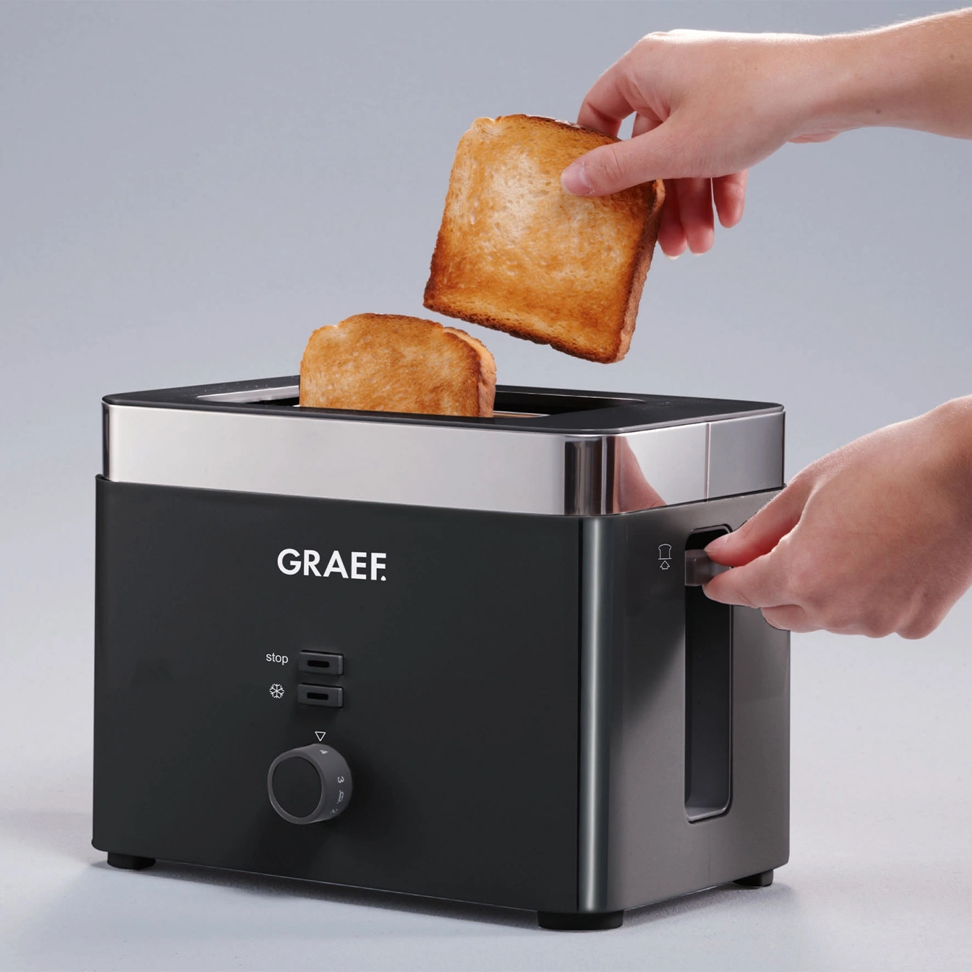 A toaster with two slices of toast being removed. A hand is operating the toaster.