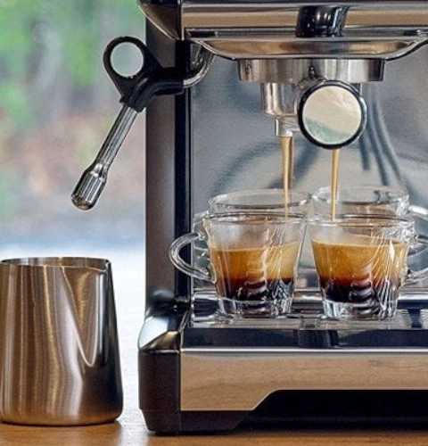 Machine à expresso versant du café dans deux tasses en verre, gros plan.
