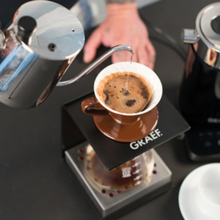 Kaffee wird in einer Tasse aufgebrüht, die auf einem Ständer steht, mit einem Wasserkocher.