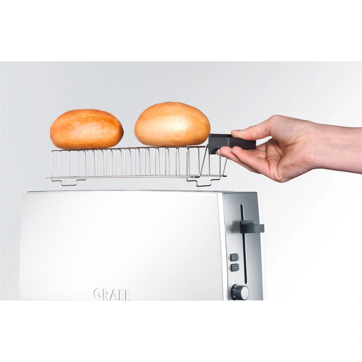 Toaster mit Brötchen und Hand, die den Toaster bedient, weißer Hintergrund.
