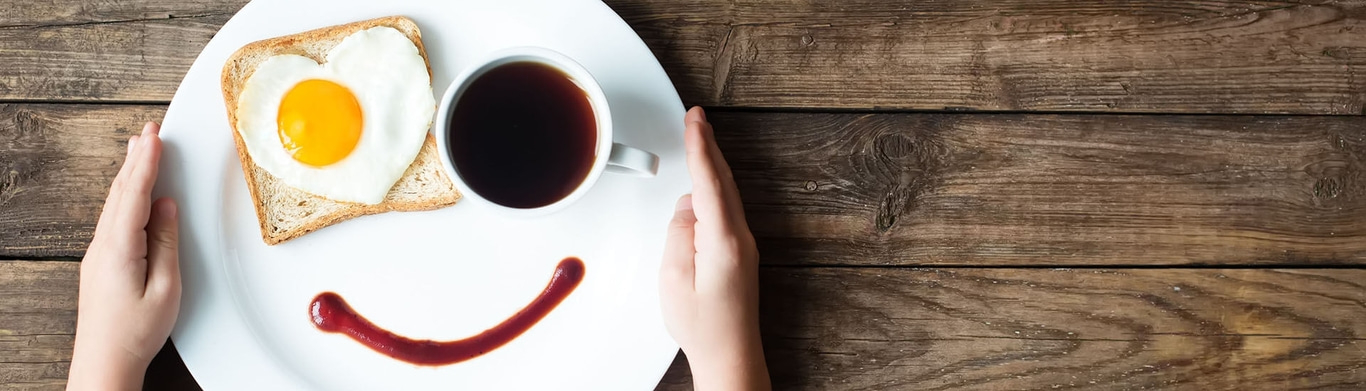 Frühstück mit Spiegelei in Herzform, Kaffee und Ketchup-Lächeln auf Holzuntergrund