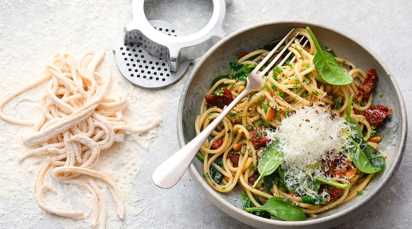 Pasta-Gericht mit Tomaten, Spinat und Käse, mit Gabel in einer Schüssel.